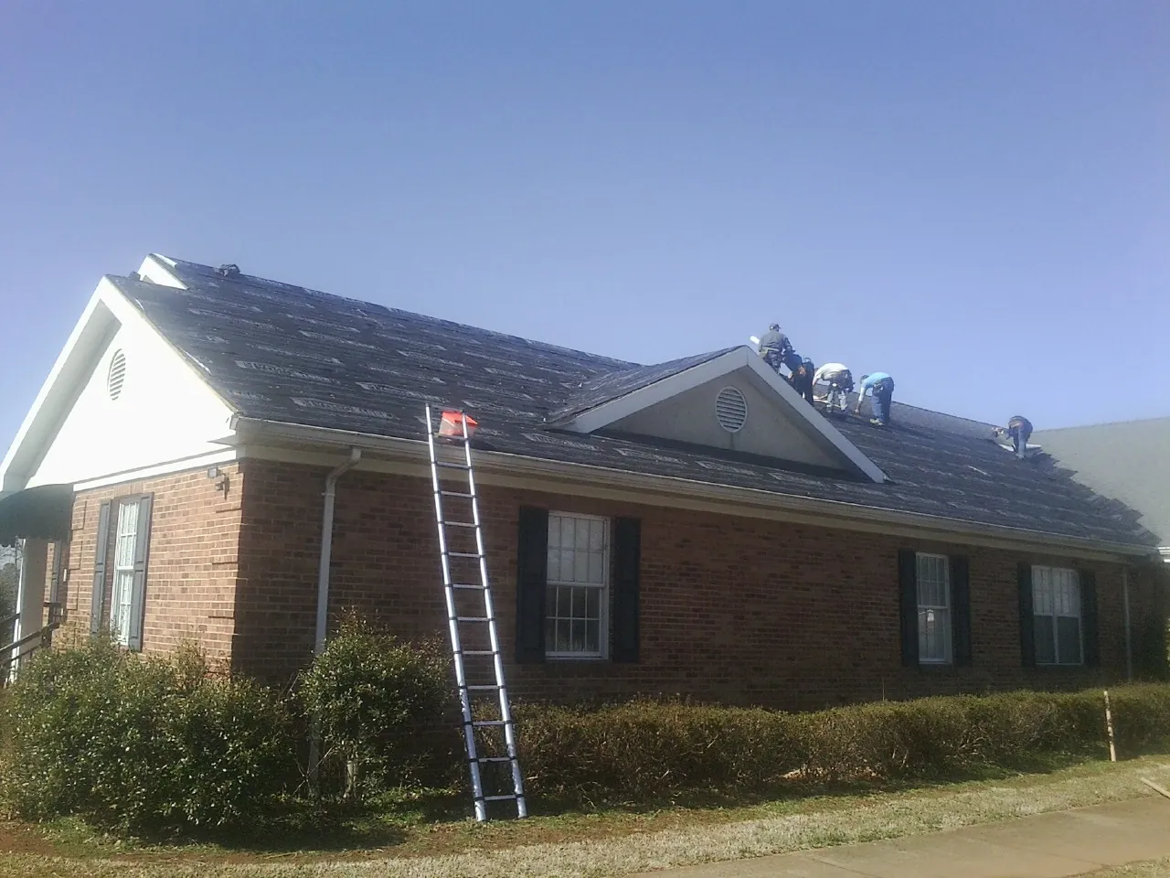 Crew tearing shingles off a brick ranch roof with a ladder set — Emergency Roof Repair work by our crew in Santa Clarita