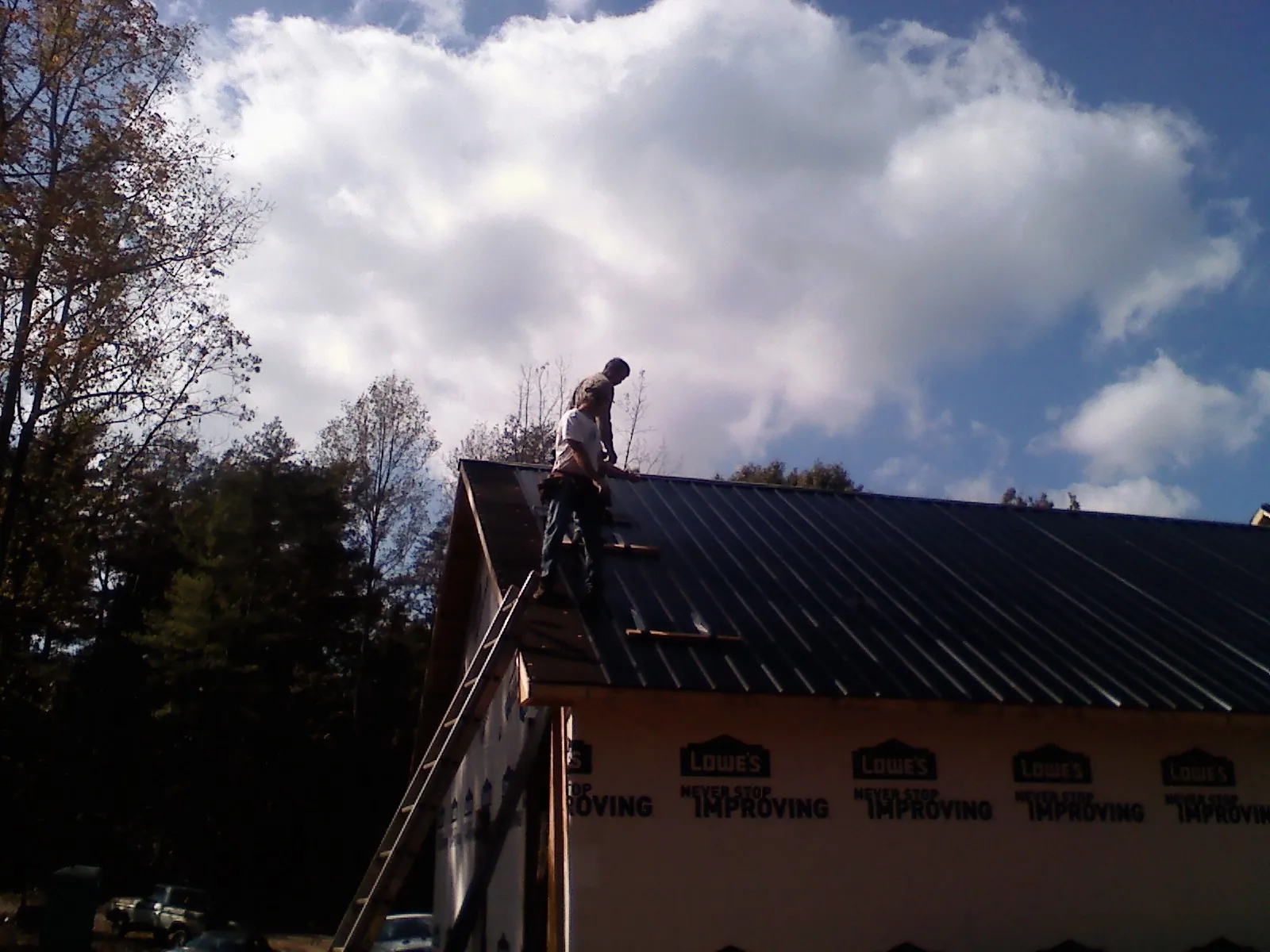 Roofer fastening dark metal panels high against a cloudy sky, from a Roof Inspection job in Santa Clarita