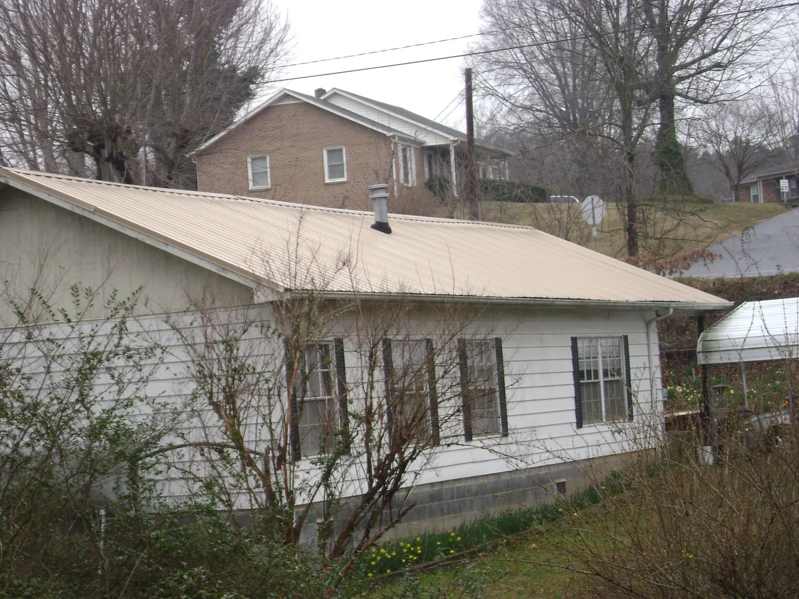 Tan metal roof on a white sided house set into a hillside — Commercial Roofing by Roofing Brothers in Santa Clarita