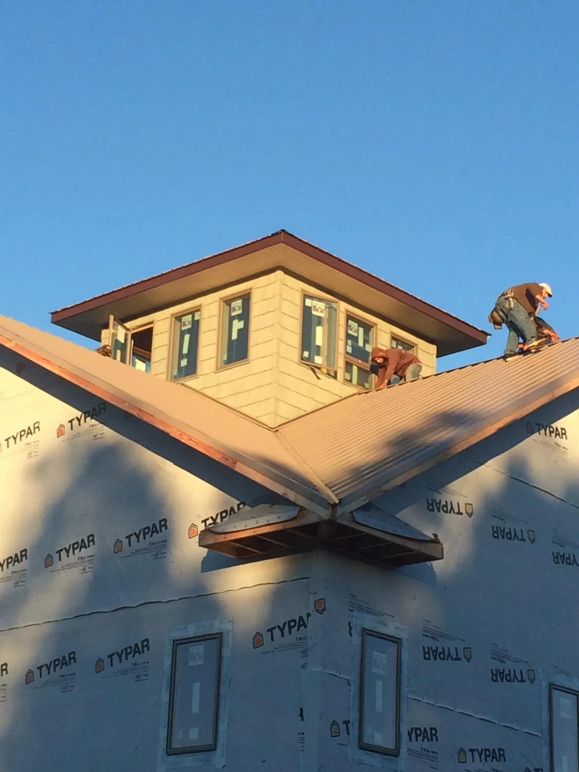 Roofers working around a rooftop cupola on a new metal roof at sunset — Roof Waterproofing in Santa Clarita by Roofing Brothers